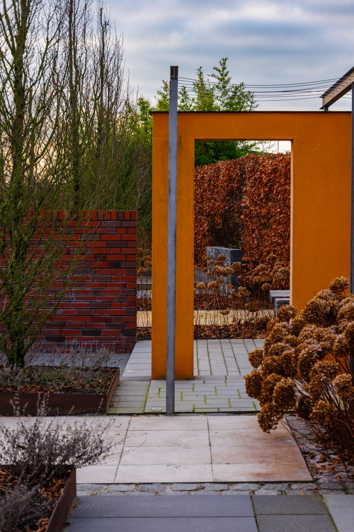 services-01 A modern garden entrance featuring vibrant orange and brick structures surrounded by autumn foliage.